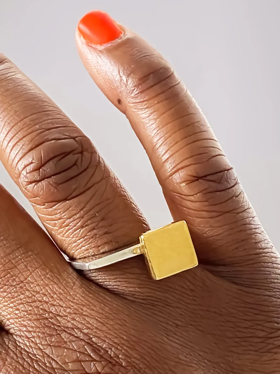 Hand wearing stacked square-top signet rings in gold and silver