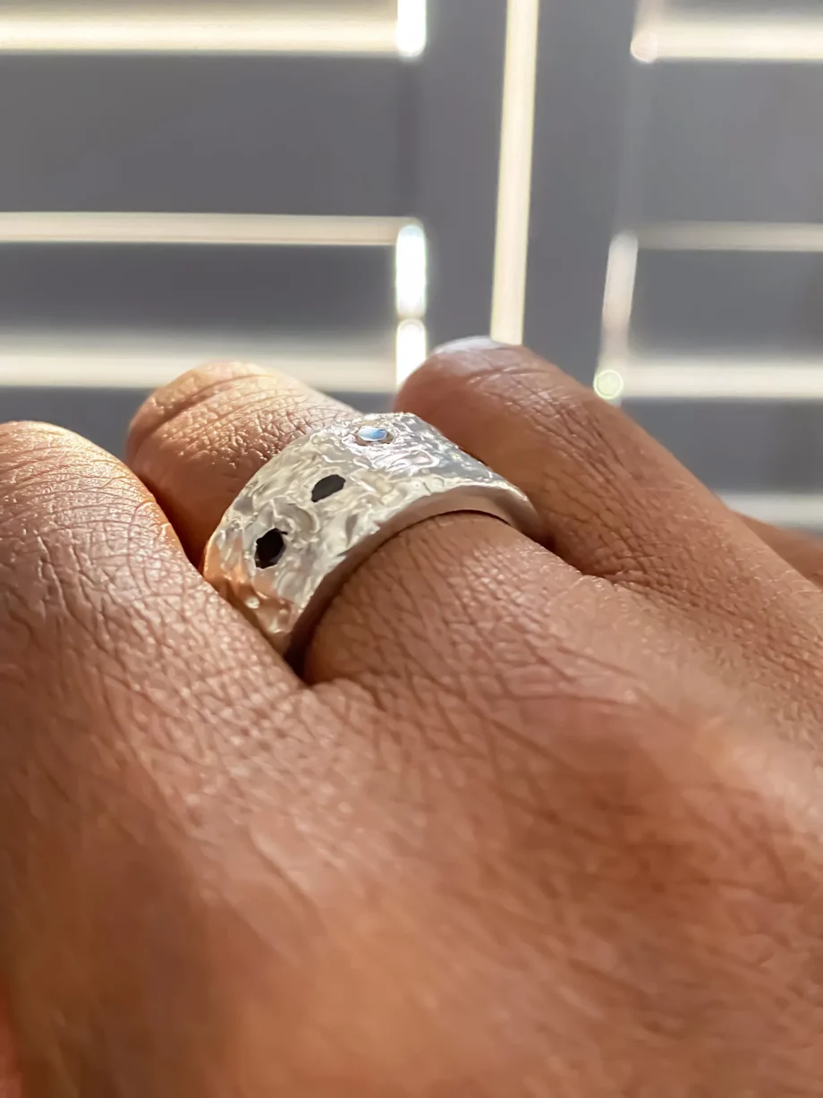 Hand wearing a silver stone set band ring with a textured finish and black gemstones.