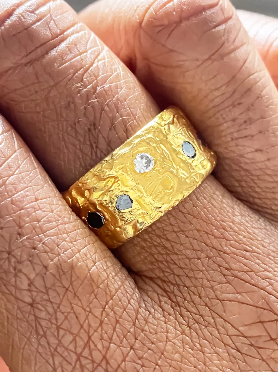 Hand wearing gold band ring with textured finish and gemstone insets.