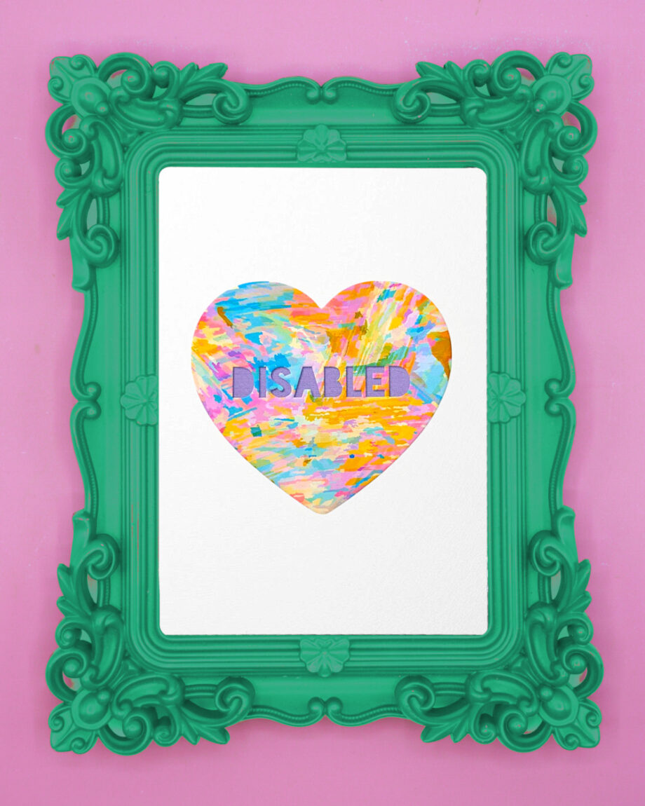 An art print featuring a heart with the word "DISABLED" in capital letters. The heart is filled with colourful, painterly textures. It’s framed in a playful ornate green frame against a soft pink background.