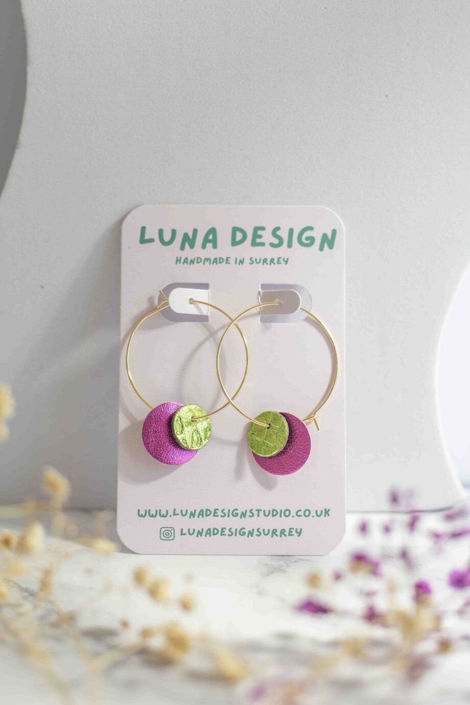 Close-up of pink and green leather circle earrings on 30mm gold-plated hoops, showing texture and stitching detail.
