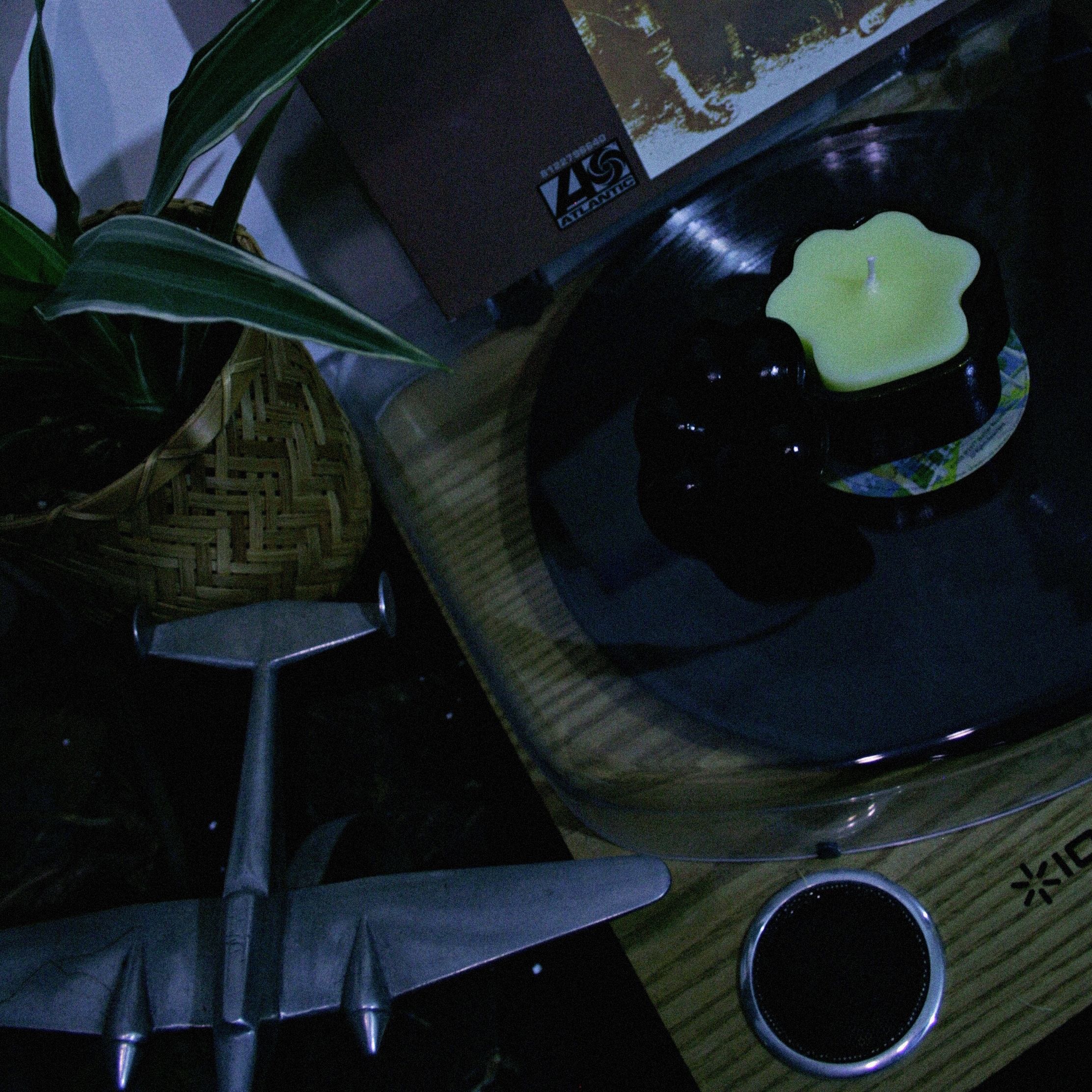 Paw-shaped black colour box with a paw-shaped yellow candle inside on top of a record-player and next to a beautiful plant and metallic plane model