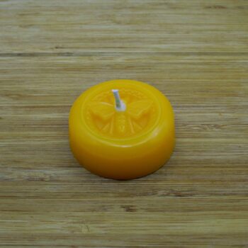 Round yellow candle with a bee imprint on a wooden background