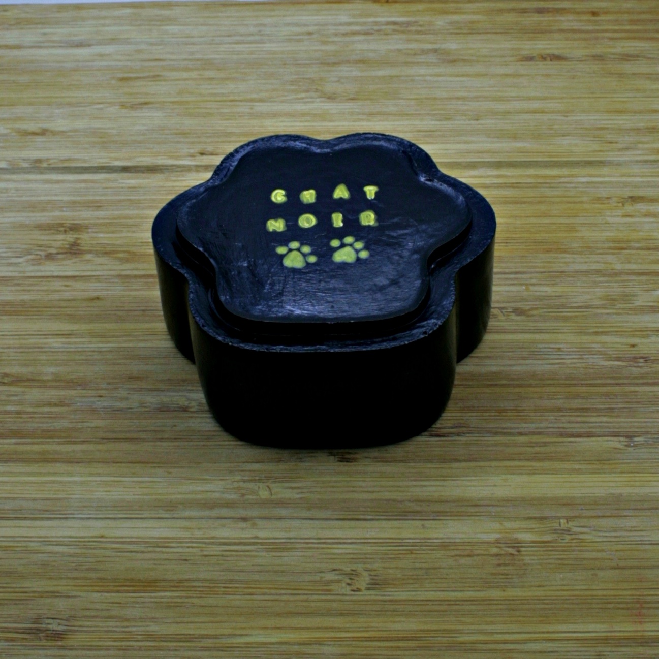 Bottom side of the black paw-shaped bow with the words Chat Noir and two paw prints written in gold colour