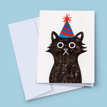 A birthday card featuring a black cat wearing a blue and red party hat with a red pom-pom on top. The cat has large, round eyes and a small, white nose.