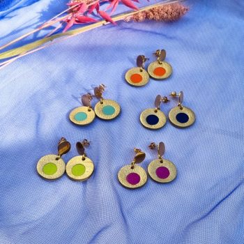 Five pairs of circular leather drop earrings in gold, featuring colourful centre inlays in orange, mint, navy, lime, and magenta, arranged on blue mesh fabric.